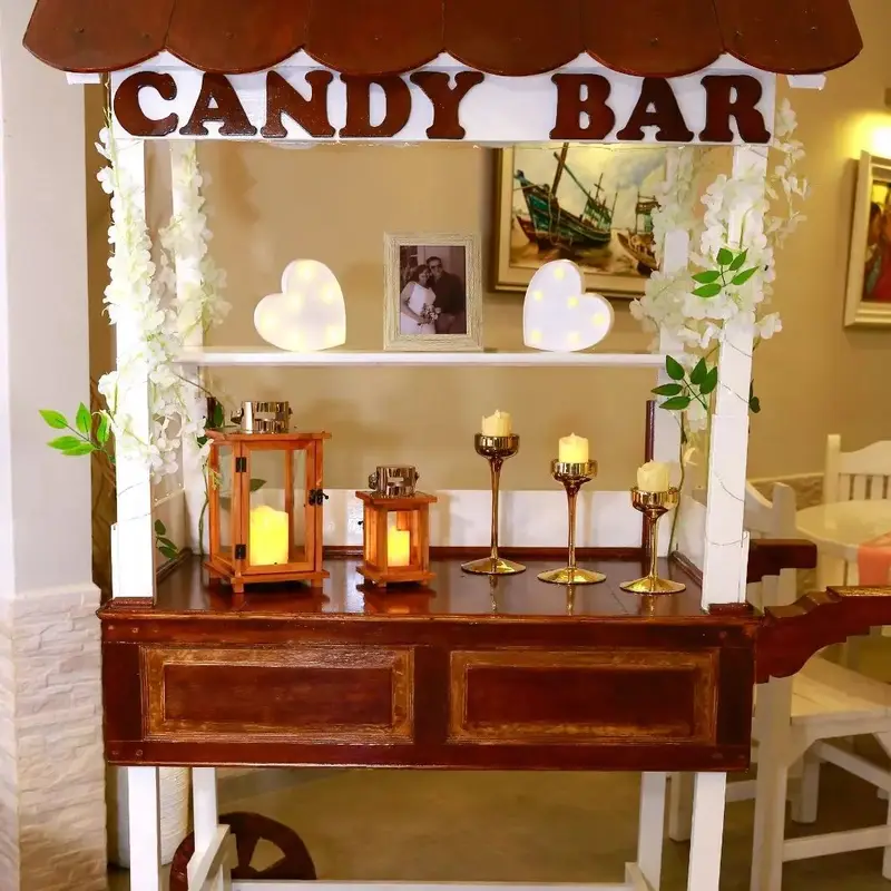 Carrito de candy bar de madera con flores blancas, velas y un cuadro