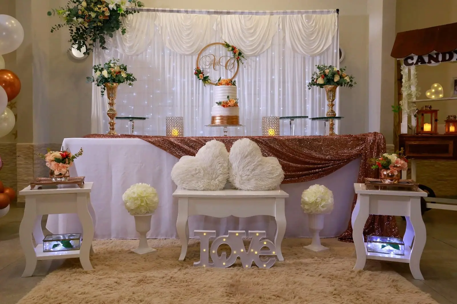 Mesa principal de un evento con cortina blanca, torta de pisos, flores y velas