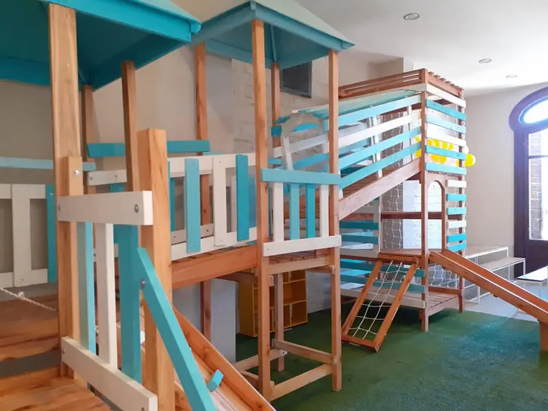 Estructura de juegos de madera con tobogán, torres con techo turquesa y red para trepar