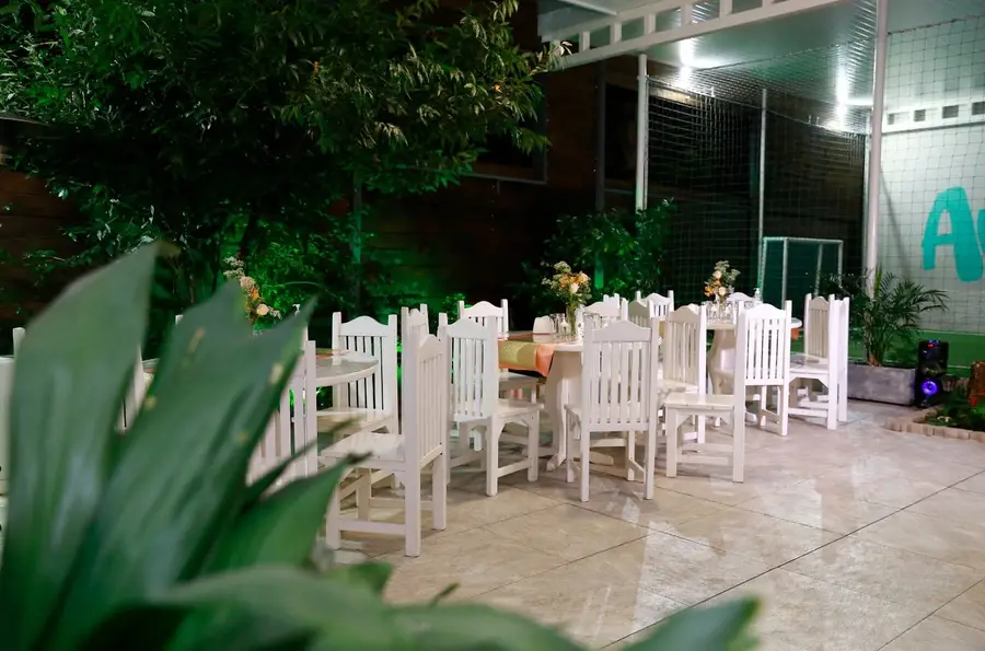 Patio de noche con mesas y sillas blancas rodeadas de plantas