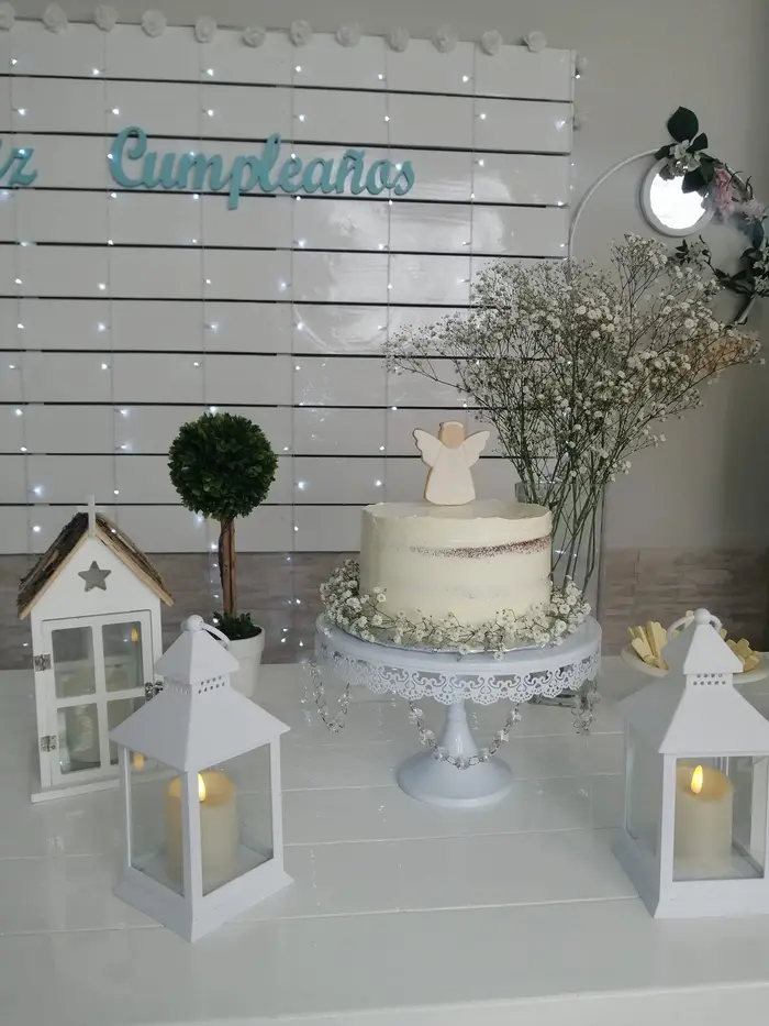 Torta blanca con un angelito, faroles y árboles de boj para un bautismo