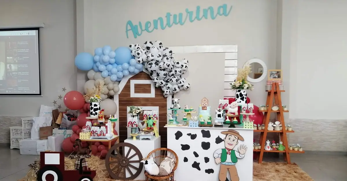 Mesa temática de granja con granero de madera, vaquitas, globos celestes y el cartel de Aventurina
