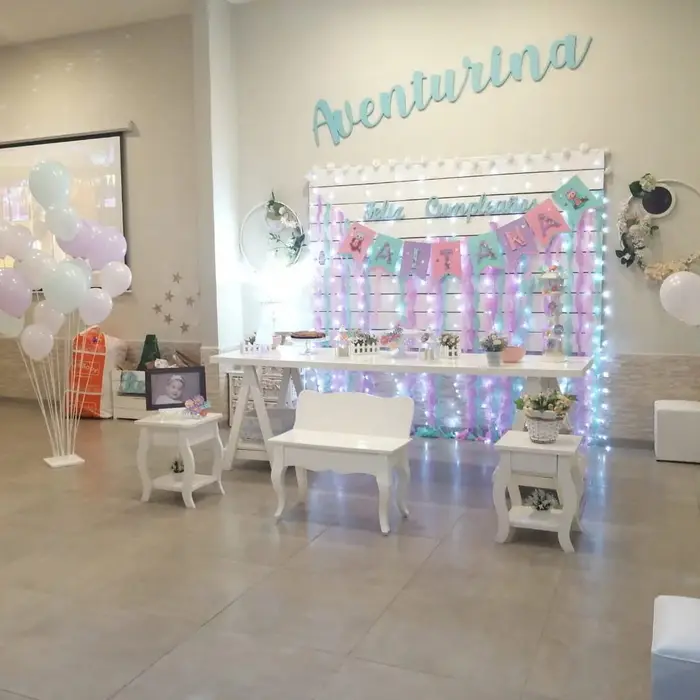 Salón decorado con cortina de luces, globos pastel y mesa principal blanca